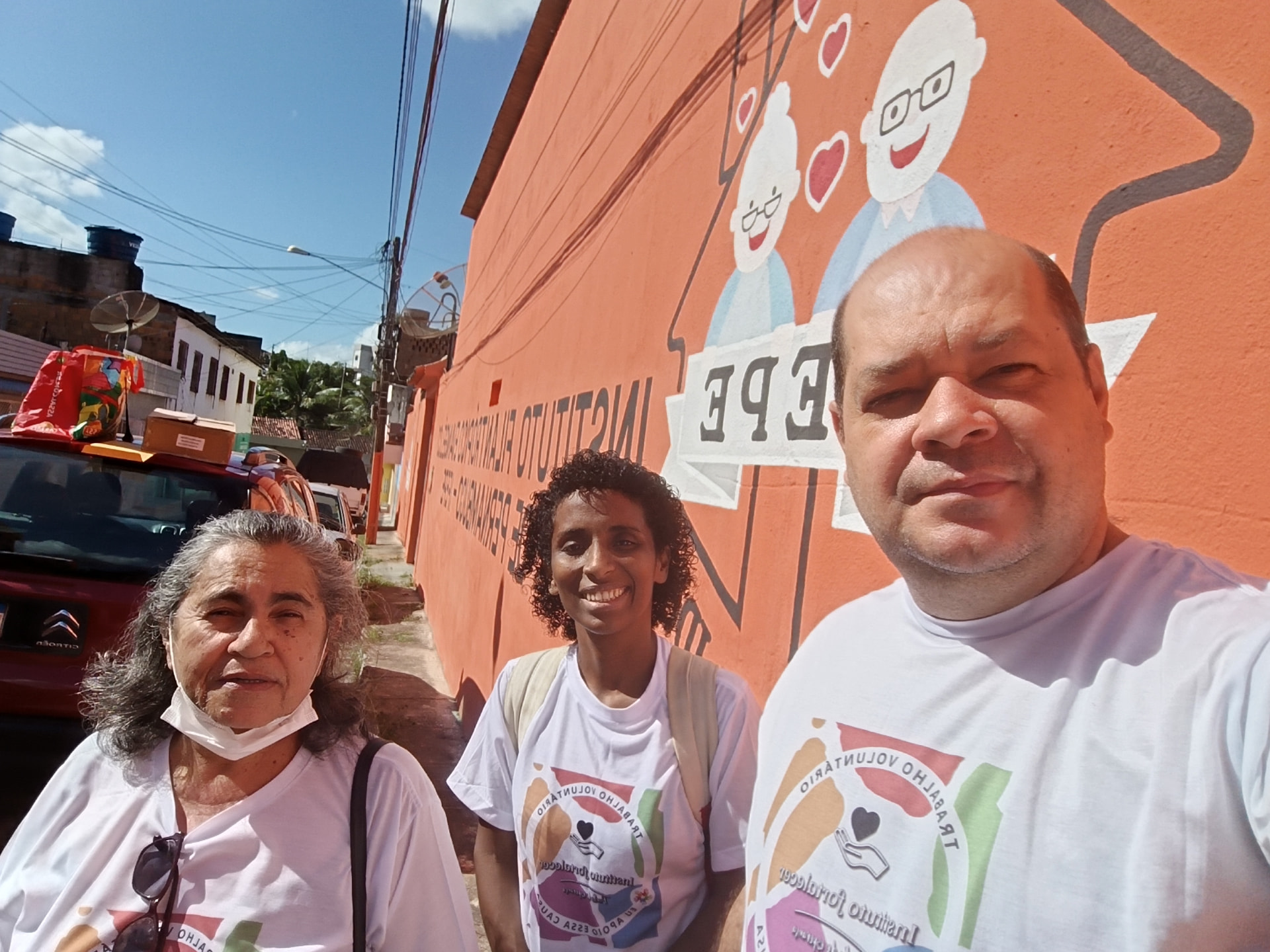 Três voluntários do Instituto Fortalecer em frente a muro pintado de instituto filantrópico