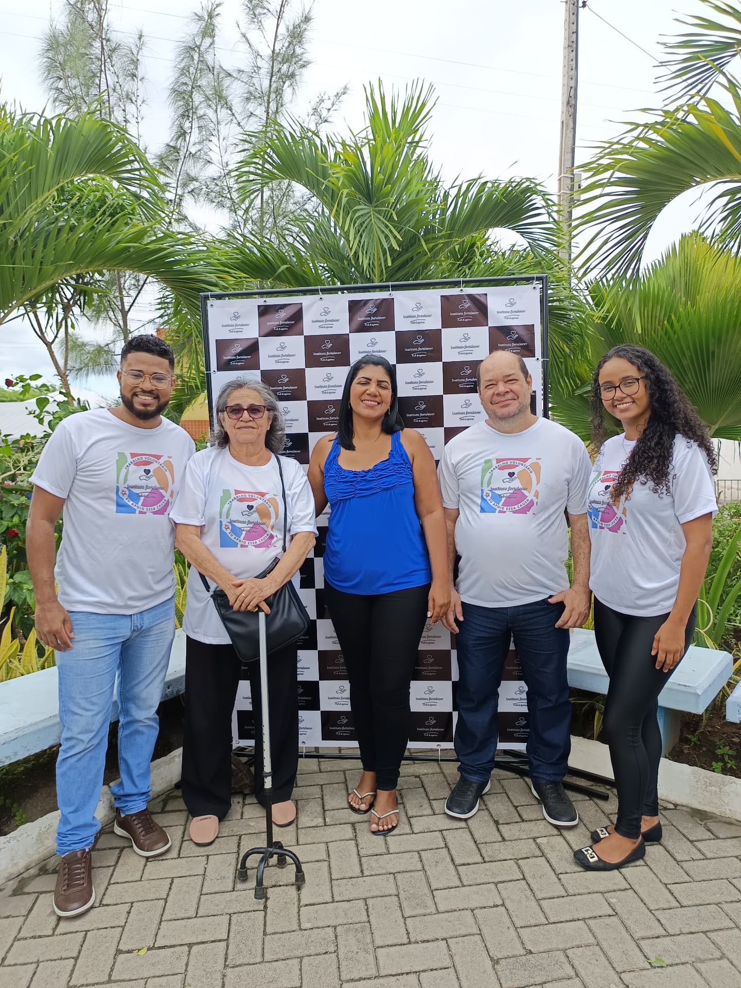 Cinco integrantes do Instituto Fortalecer posando diante do painel institucional ao ar livre